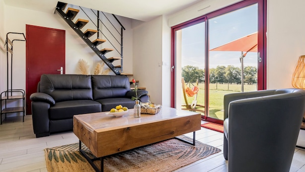 A modern living room with a black leather sofa, a wooden coffee table, a staircase, and a large sliding glass door leading to an outdoor area. - Peaceful cottage near Nantes - 4 guests (Ligné)