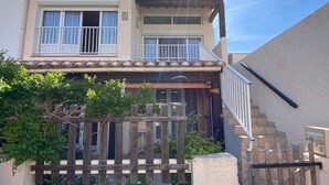 Un edificio de dos pisos con un balcón, una valla de madera y una escalera que lleva a la entrada.