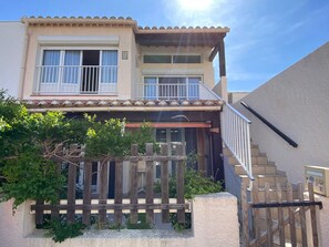 A two-story building with a balcony, a wooden fence, and a staircase leading to the entrance. - Air-conditioned apartment near sea - 6 guests (Port Leucate)