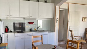 Una cocina compacta con armarios blancos, un lavamanos, un hervidor rojo y una zona de comedor con mesa y sillas.