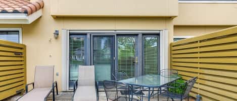 A patio with a glass table and chairs, a yellow gate, and a sliding glass door.