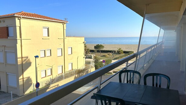 Ein Balkon mit Tisch und Stühlen, der Blick auf Strand und Gebäude bietet.