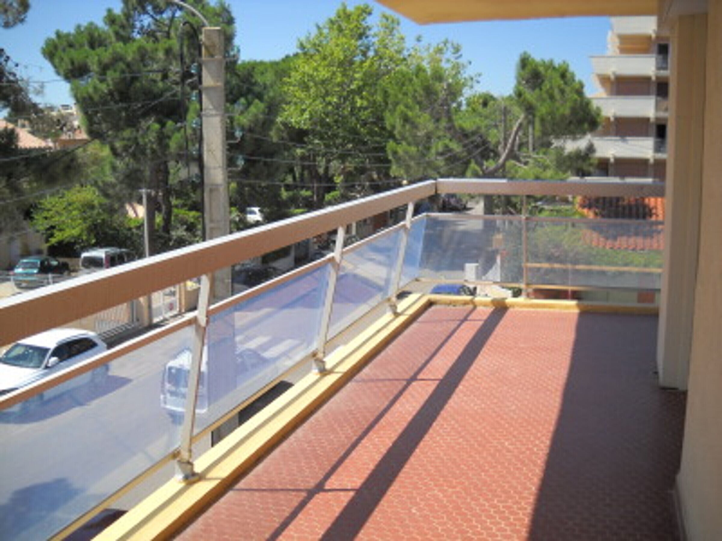 Varanda com guarda-corpo de vidro, com vista para uma rua com carros estacionados e árvores.