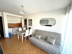 A compact living space with a dining area, kitchenette, and a sofa with patterned cushions. - Beachfront apartment, parking - 4 guests (Argelès-sur-Mer)