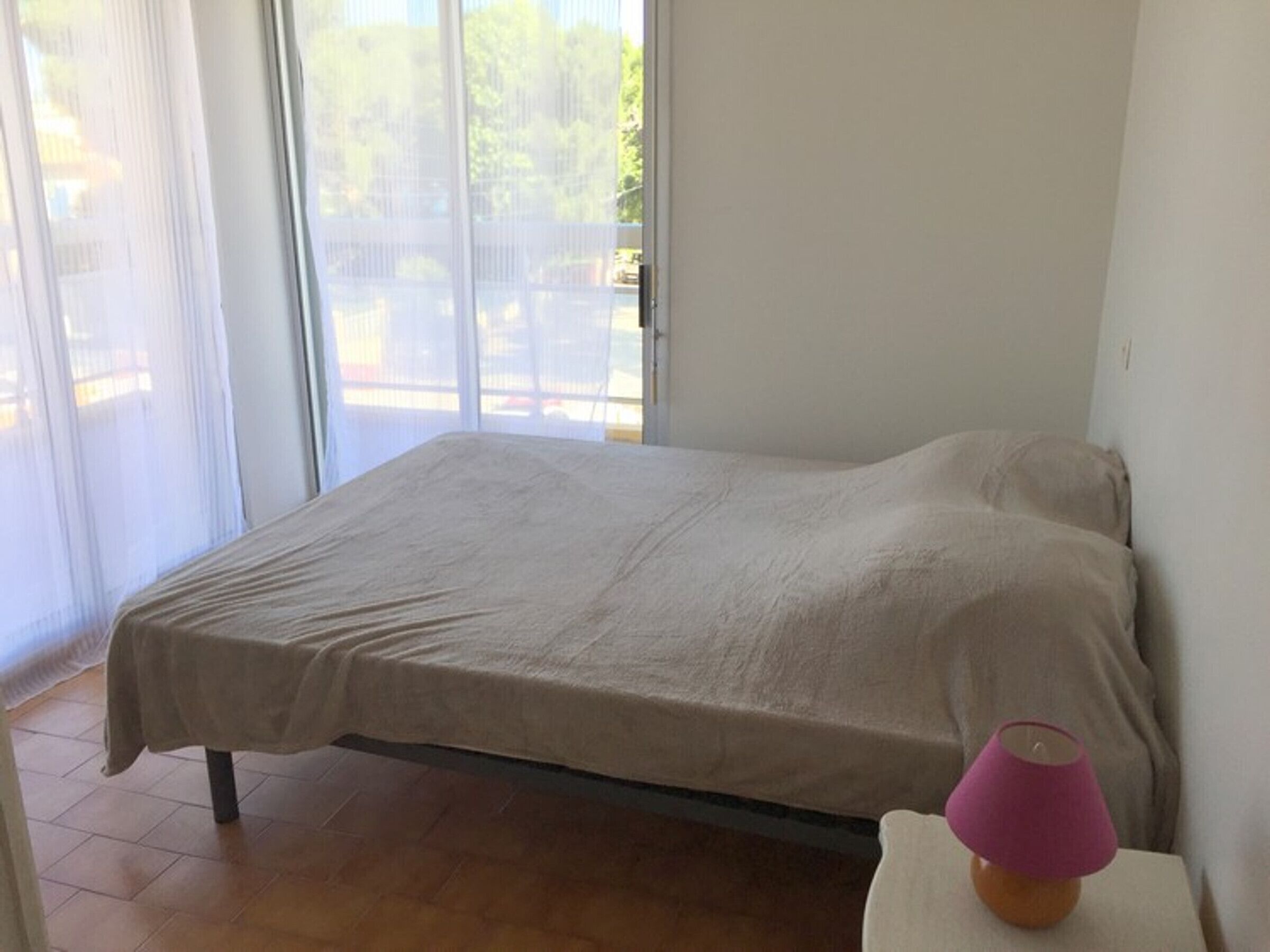 A bedroom with a bed, a nightstand, and a window with a view of the outdoors.