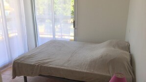 Ein Schlafzimmer mit einem Bett, einem Nachttisch und einem Fenster mit Blick ins Freie.