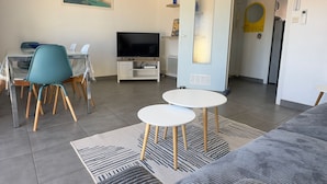 Een moderne woonkamer met een televisie, een eethoek en een deur naar een andere kamer.