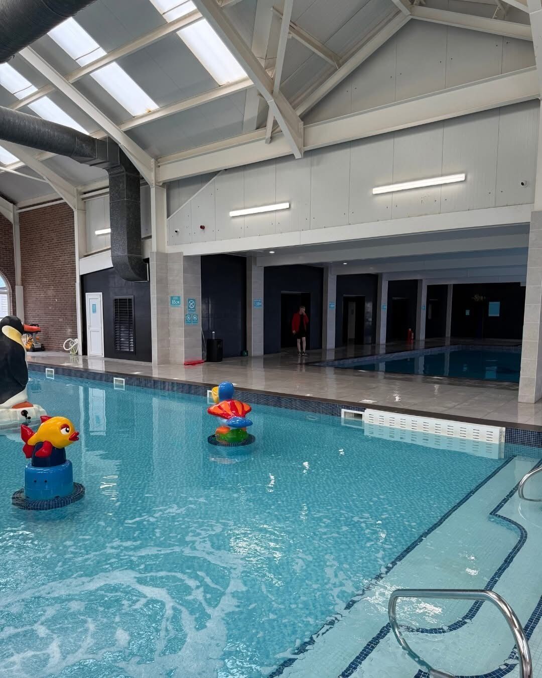 Ein Hallenbad mit klaren Bahnen, einem Sprungturm und einem Kinderspielbereich mit aufblasbaren Spielzeugen.