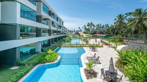 Et moderne hotel med swimmingpool, udendørs siddepladser og frodig beplantning.