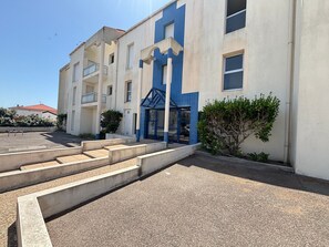 A multi-story building with a blue entrance, concrete steps leading up to it, and a clear sky. - Studio with large terrace, sea view - 2 guests (Les Sables-d'Olonne)