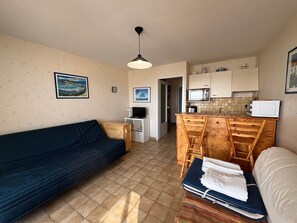 A compact living space with a sofa, a small dining table with chairs, a kitchenette with a microwave, and a television. - Studio with large terrace, sea view - 2 guests (Les Sables-d'Olonne)