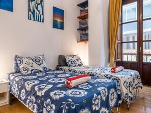 A room with two beds, a wooden floor, a window with curtains, and artwork on the walls. - Cozy apartment in the heart of Granada - 4 guests (Granada)