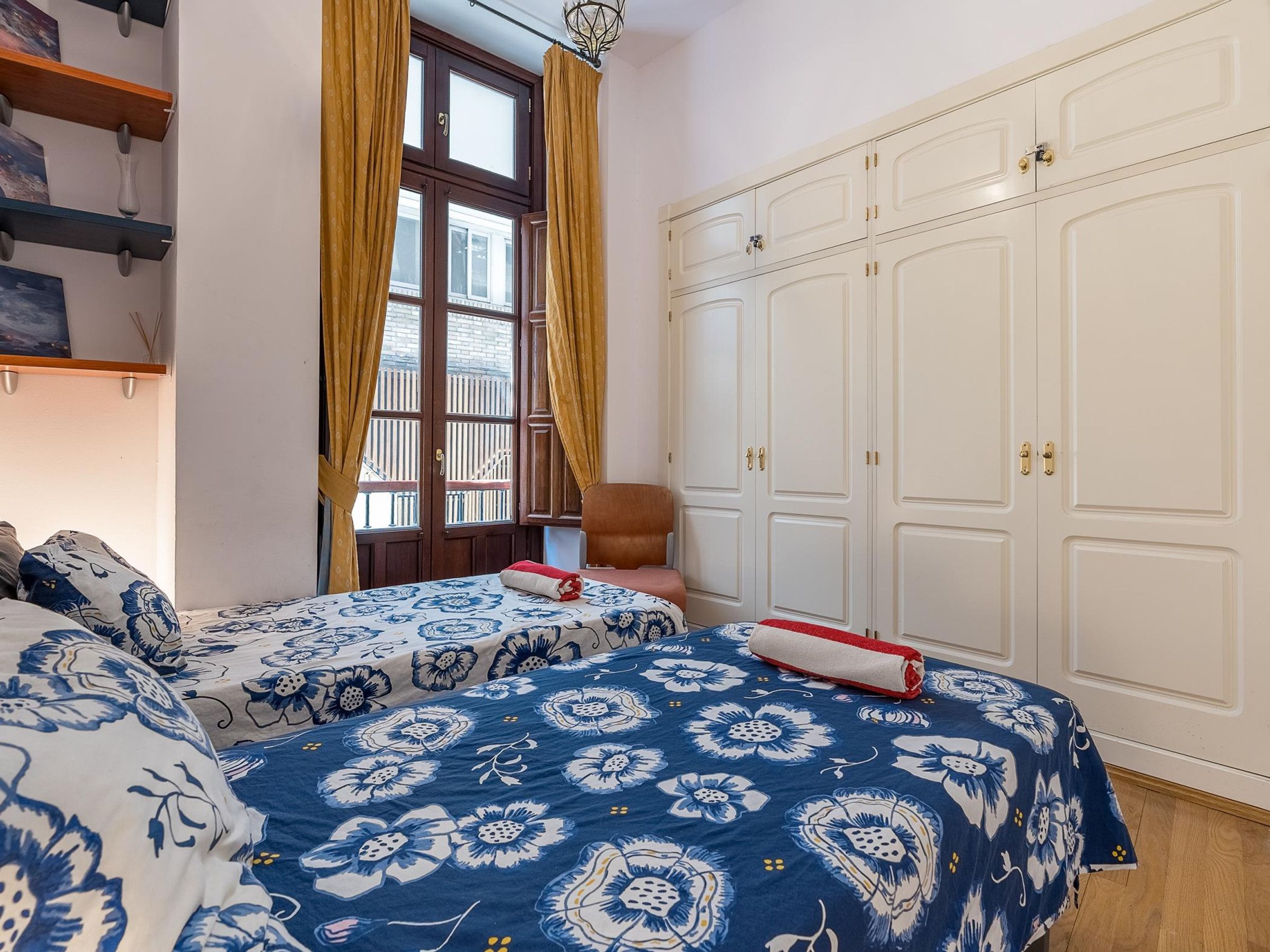 A bedroom with two beds, a wardrobe, and a window with curtains.
