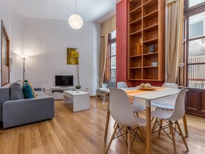 Ein modernes Wohnzimmer mit einer Couch, einem Fernseher, einem Esstisch, Stühlen und einem Bücherregal.