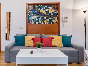 A modern living room with a grey sofa, colorful cushions, a white coffee table, a potted plant, and a decorative wall piece. - Cozy apartment in the heart of Granada - 4 guests (Granada)