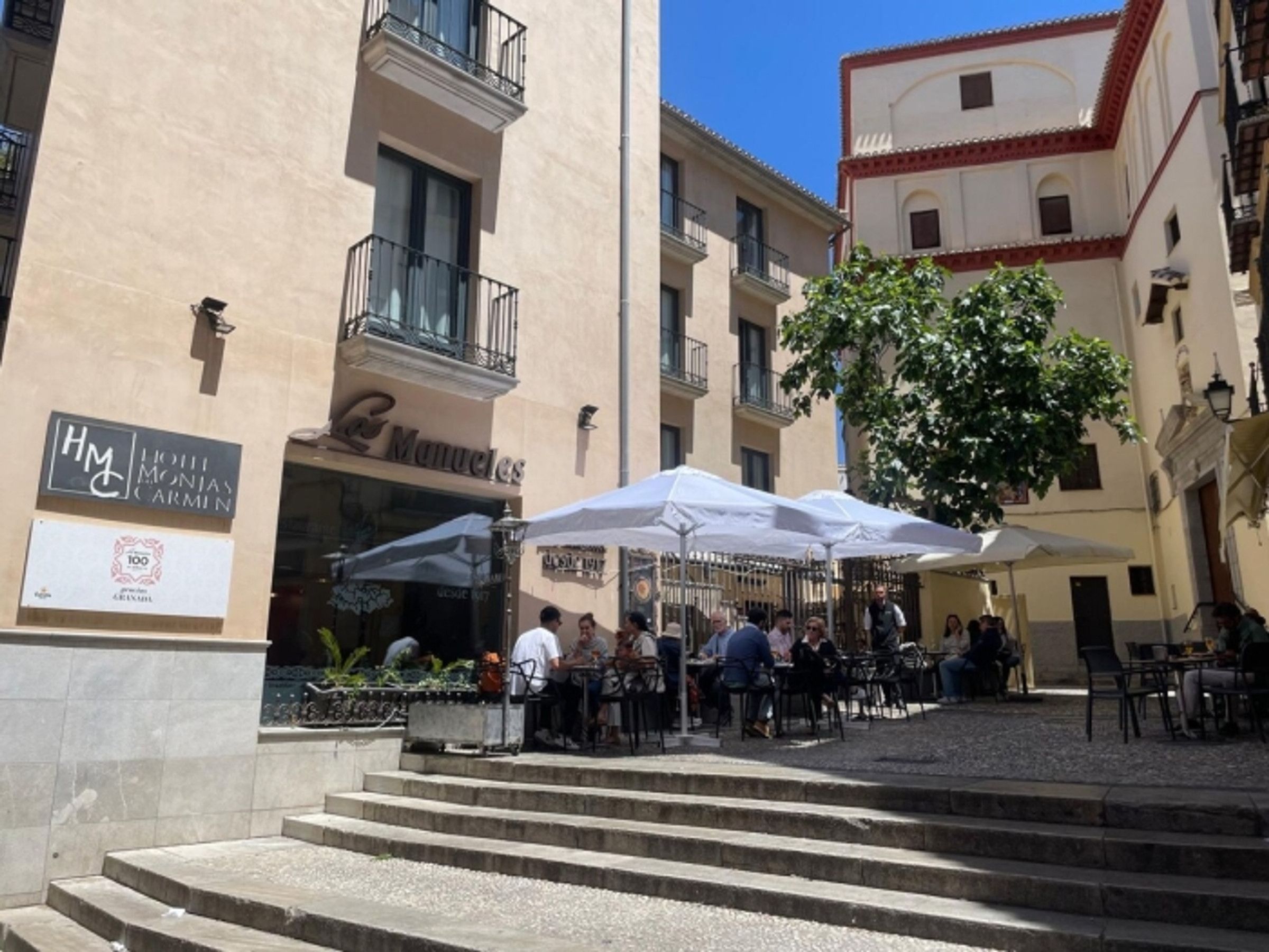 A courtyard with outdoor seating, a hotel named 'Manuels,' and a sign for 'HM Hotel Monjas Carmín.'