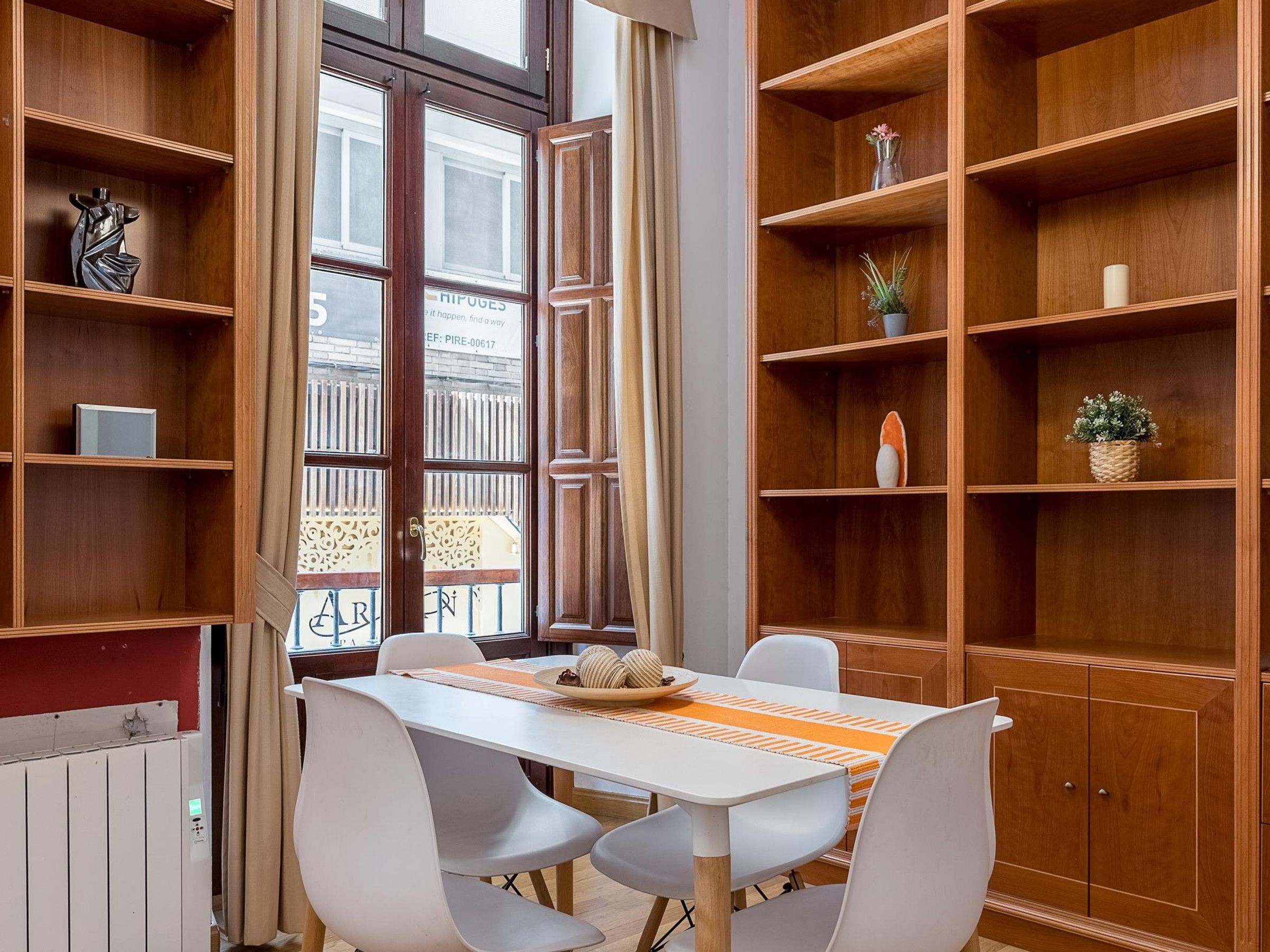 A dining area with a table, chairs, and wooden shelves with various items.