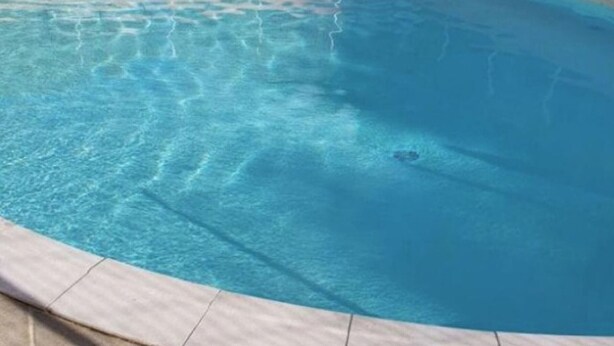 Ein klares Schwimmbecken mit gefliestem Rand und einem Stuhl in der Nähe.