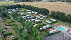 Ein Caravanpark mit ordentlich angeordneten Wohnwagen, einem Schwimmbad und einem weitläufigen Feld im Hintergrund.