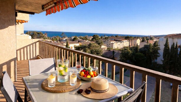 A balcony with a table set for two, overlooking a coastal town. - Quiet apartment, sea view - 4 guests (Saint-Aygulf)