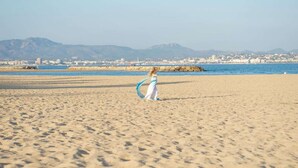 A beach with a person holding a blue object, a clear sky, and distant buildings. - Quiet apartment, sea view - 4 guests (Saint-Aygulf)