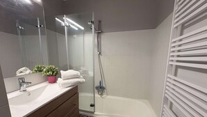 Ein modernes Badezimmer mit einer gläsernen Duschkabine, einer weißen Badewanne, einem Holzwaschtisch und einer Topfpflanze.