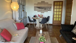 A living room with a sofa, a dining table with chairs, a coffee table with a plant, and a door with a frosted glass panel. - Quiet apartment, sea view - 4 guests (Saint-Aygulf)