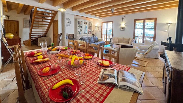 Un comedor con mantel a cuadros rojos, vigas de madera, una escalera y vistas al exterior.