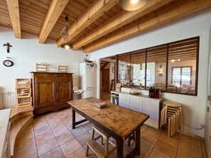 Une cuisine rustique avec des poutres en bois, une grande fenêtre et un coin repas comprenant une table et des chaises en bois.