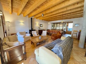 Un salon chaleureux avec des poutres apparentes, une cheminée et un coin repas comprenant des chaises et une table.