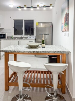 Une cuisine moderne dotée d’un plan de travail en granit, d’appareils électroménagers en acier inoxydable et d’un coin bar avec des tabourets.
