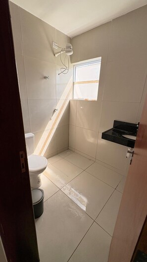 A bathroom with a toilet, shower, and a small window.