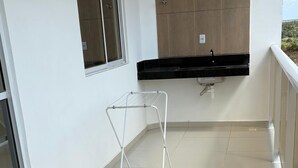 A balcony with a tiled floor, a window, a wall-mounted air conditioning unit, and a white metal drying rack. - Apartment in Jacumã (Balneário Novo Mundo, Praia de Jacuma, Conde)