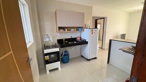 A compact kitchen with a gas stove, oven, sink, and a white refrigerator. - Apartment in Jacumã (Balneário Novo Mundo, Praia de Jacuma, Conde)