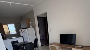 A modern living room with a flat-screen TV, a wooden entertainment unit, and a dining area with a table and chairs. - Apartment in Jacumã (Balneário Novo Mundo, Praia de Jacuma, Conde)