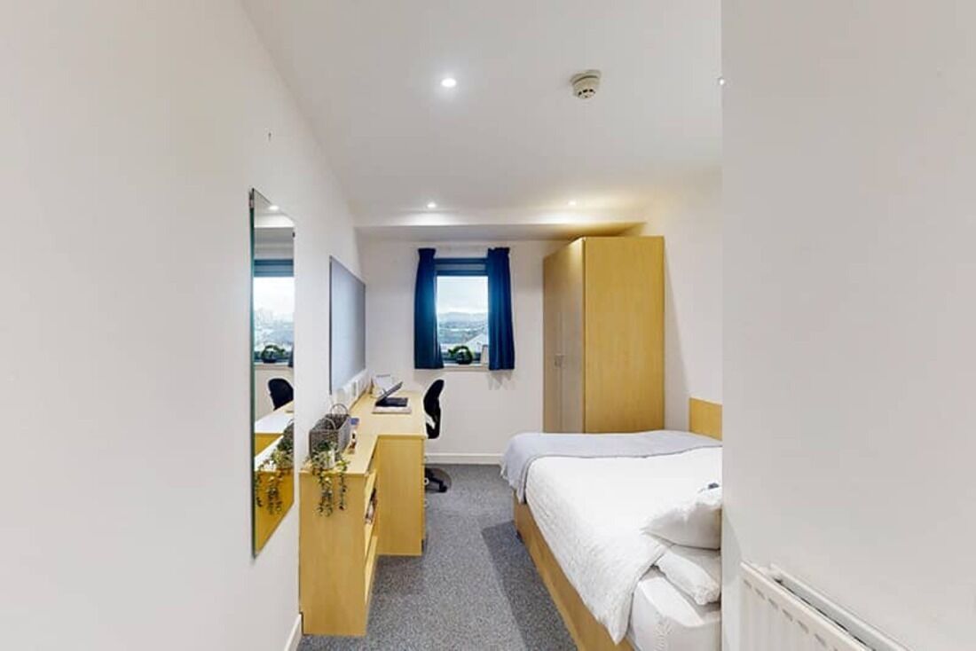 A bedroom with a bed, a desk, a chair, a wardrobe, and a window with curtains.