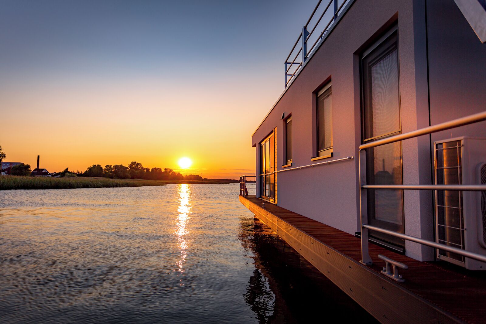 Een gebouw aan de rivier met een terras dat over het water uitsteekt, grote ramen en een balustrade.