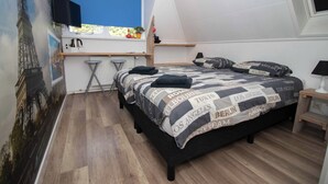 Ein Schlafzimmer mit Bett, Schreibtisch, Stuhl, Fernseher und Fenster.