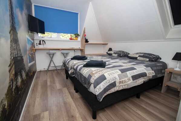 A bedroom with a bed, a desk, a chair, a TV, and a window.