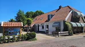 Ein traditionelles europäisches Gebäude mit Ziegeldach und einem Schild, das Wohnungen bewirbt, sowie eine gepflasterte Straße.