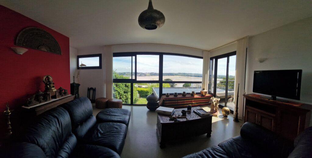 A living room with a curved ceiling, a large window with a view, a black leather sofa, a coffee table, and a television.
