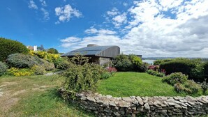 Une maison moderne avec un mur en pierre, un jardin luxuriant et une vue dégagée sur le ciel.