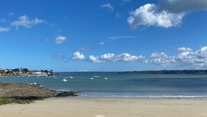 Une plage avec un ciel dégagé, une eau calme et des bâtiments qui se dessinent à l’horizon.
