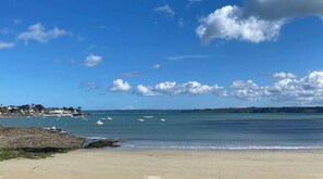 Ein Strand mit blauem Himmel, ruhigem Wasser und Gebäuden in der Ferne.