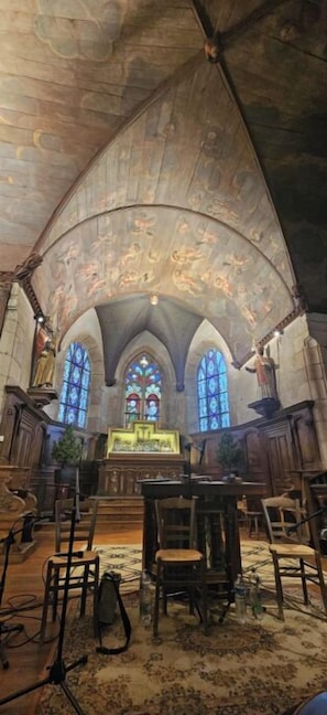 Ein Innenraum mit Rundbogenfenstern, einem hölzernen Altar und einer Gewölbedecke mit Fresken.