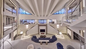 A spacious, modern interior with a central seating area, multiple balconies, and a high ceiling.