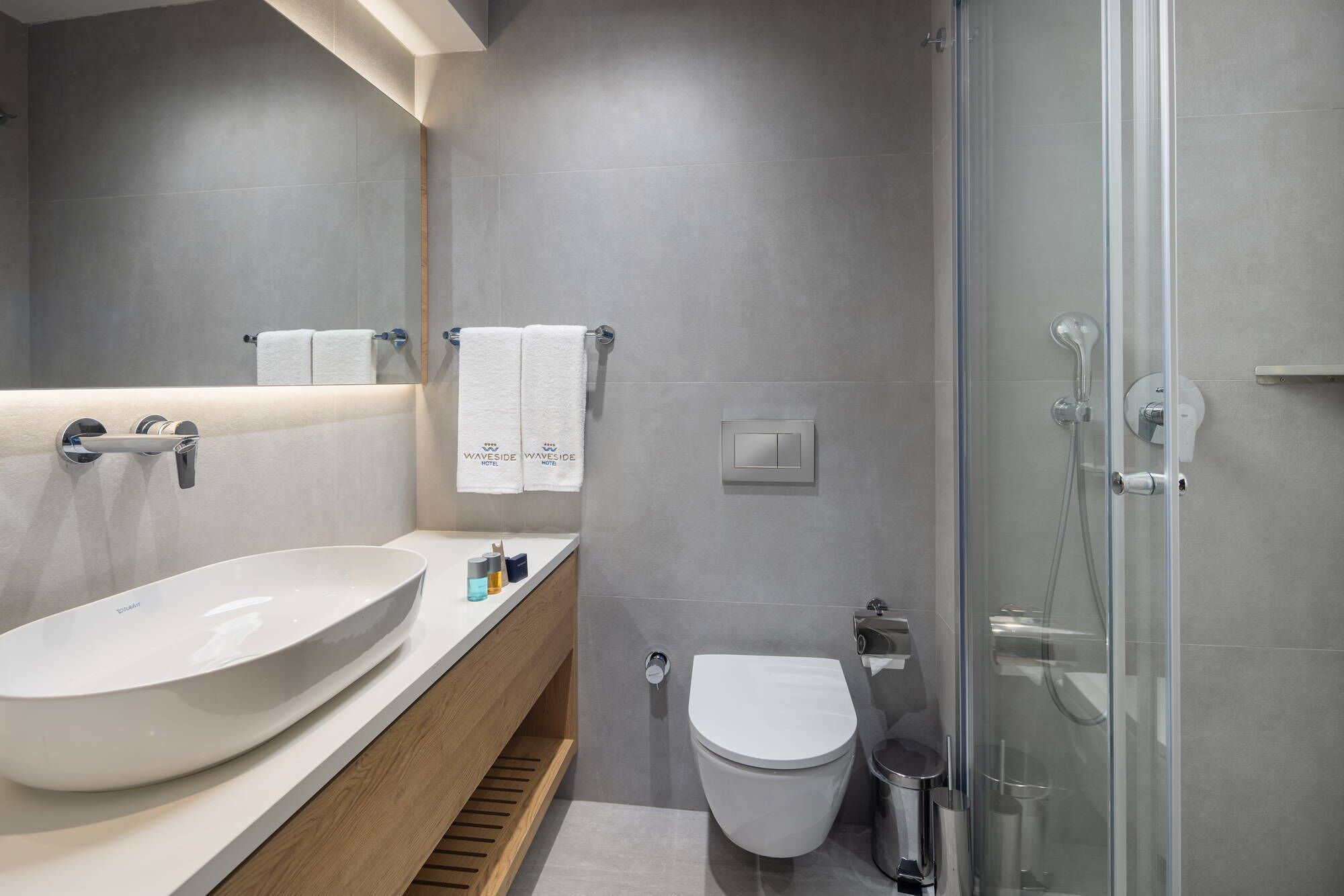 A modern bathroom with a large white sink, a toilet, and a glass shower enclosure.
