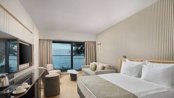 A hotel room with a bed, a sofa, a TV, a desk with a kettle, and a view of the sea.