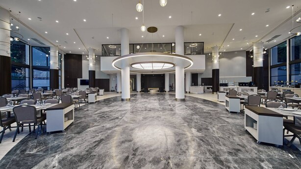 A spacious hotel lobby with a central circular light fixture, multiple seating areas, and large windows.