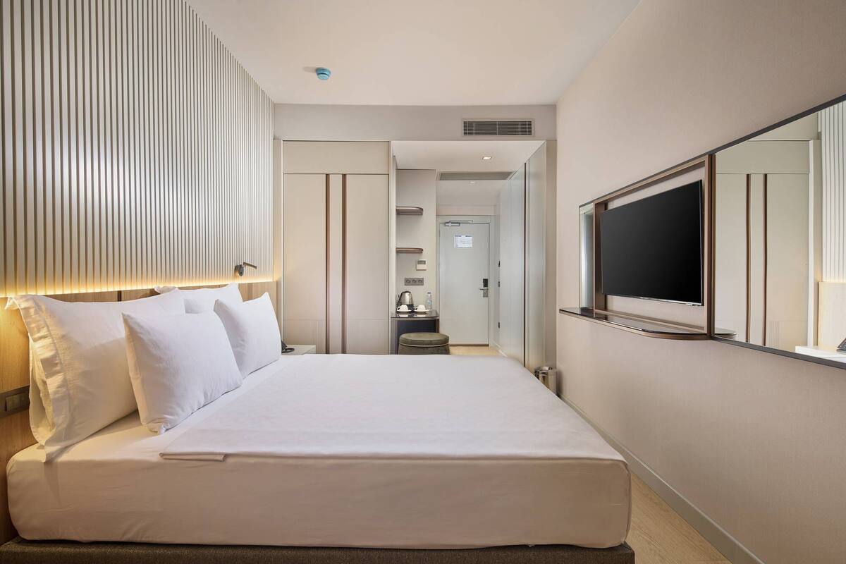 A hotel room with a large bed, a TV mounted on the wall, and a door leading to a bathroom.